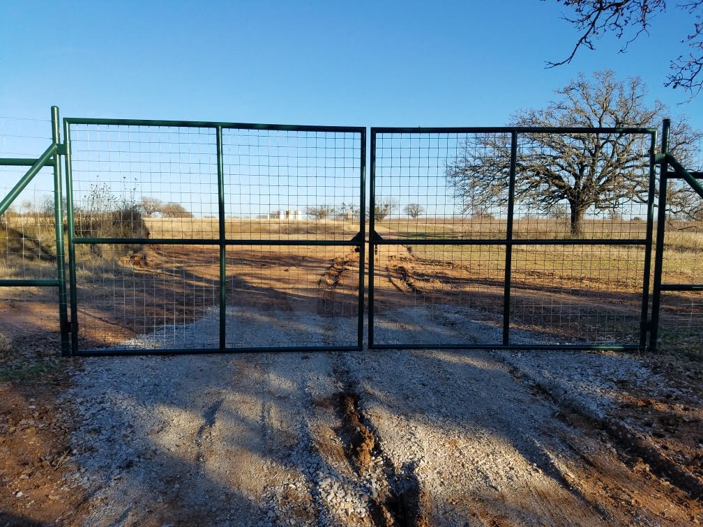 Green welded wire double drive game ranch entrance gate on caliche road — Central Texas