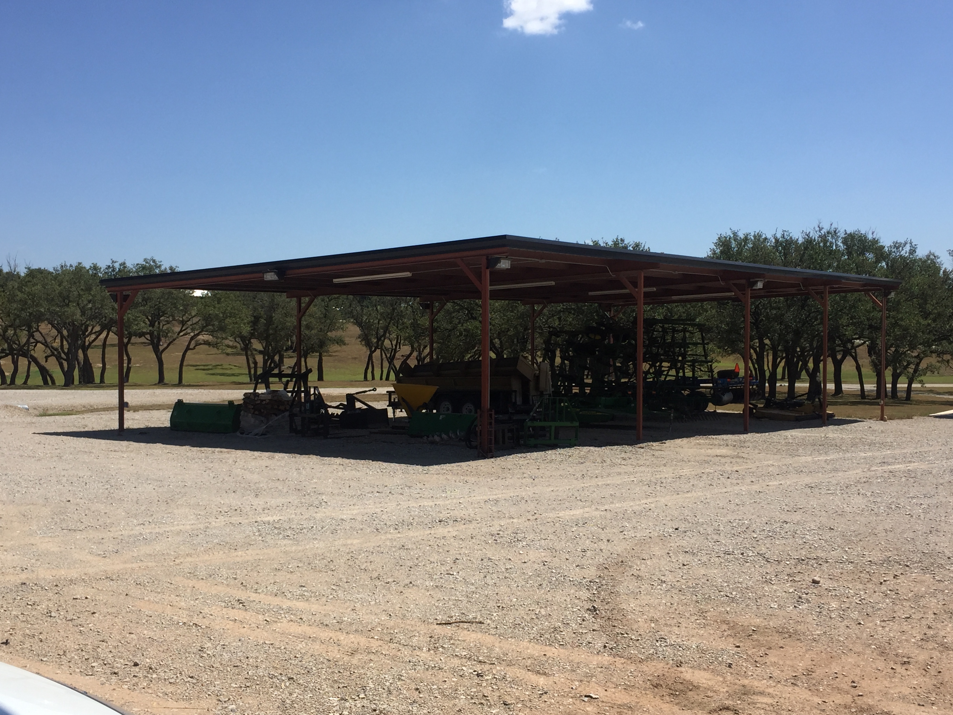 Open-sided metal equipment shed with red steel posts — Central Texas